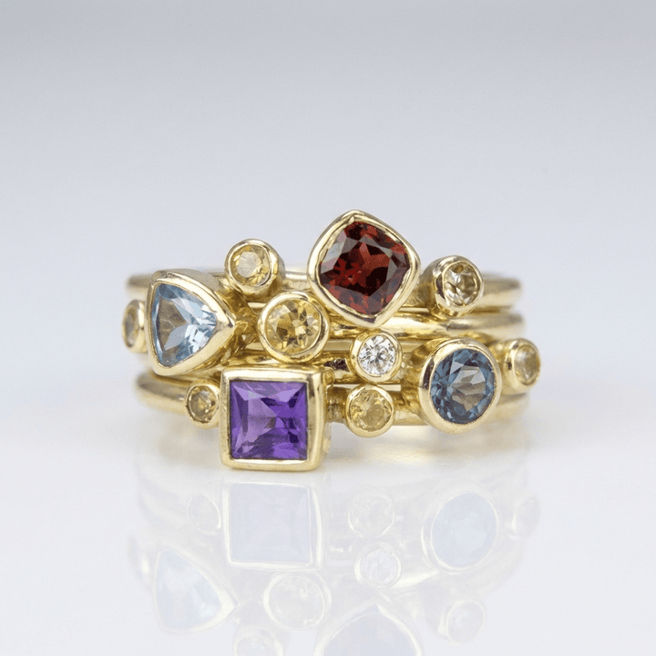 Conjunto de anéis empilhados com pedras preciosas coloridas em ouro, joias da marca Rose & Oliver, exibe detalhes vibrantes e elegantes.